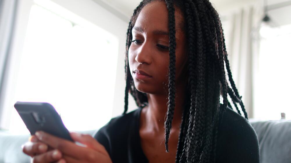 A young girl looks at the mobile phone she is holding. 