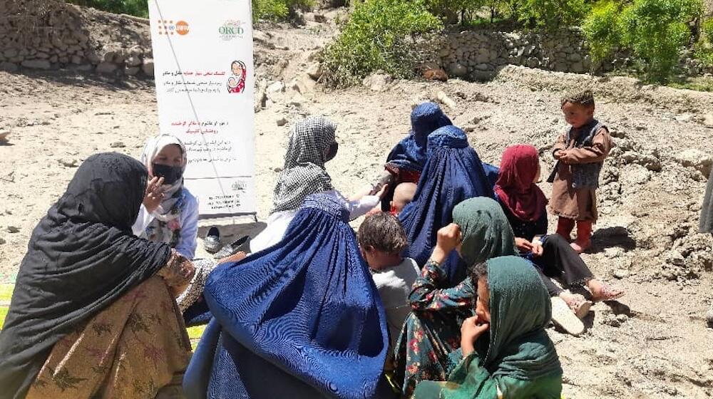 Un groupe de femmes et d’enfants discutent à l’extérieur, assis sur un terrain rocheux